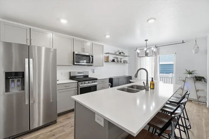 Kitchen featuring a large island with an integrated double basin sink, stainless steel appliances, light gray cabinetry, and wood-finish flooring