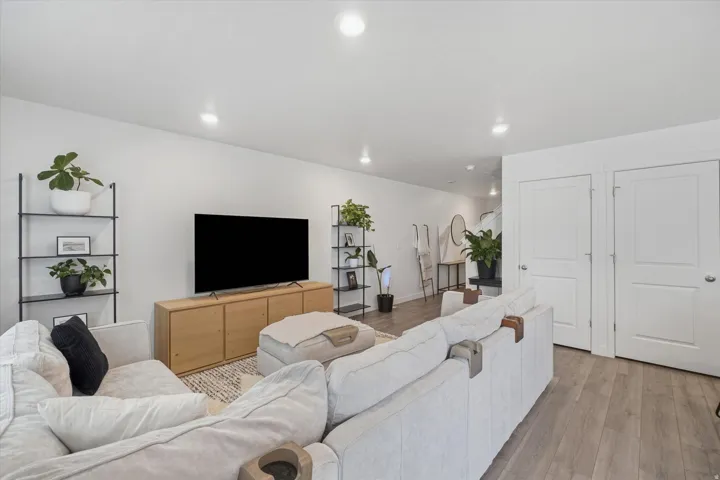 Spacious living area featuring light wood-finish flooring, recessed lighting, white walls, two paneled doors, and a built-in media console