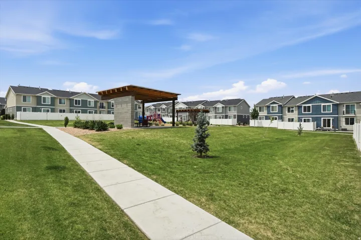 Expansive community green space featuring a paved walkway, manicured lawn, and mature trees