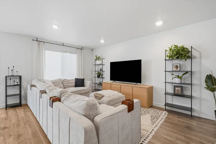 Bright living area featuring wood-finish flooring, recessed lighting, and a window with a curtain rod