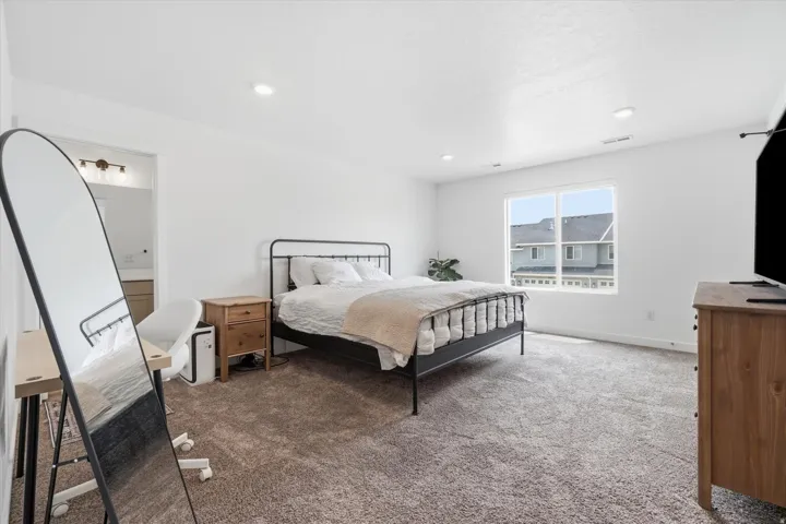 Spacious bedroom featuring plush carpeting, crisp white walls, recessed lighting, and a large window