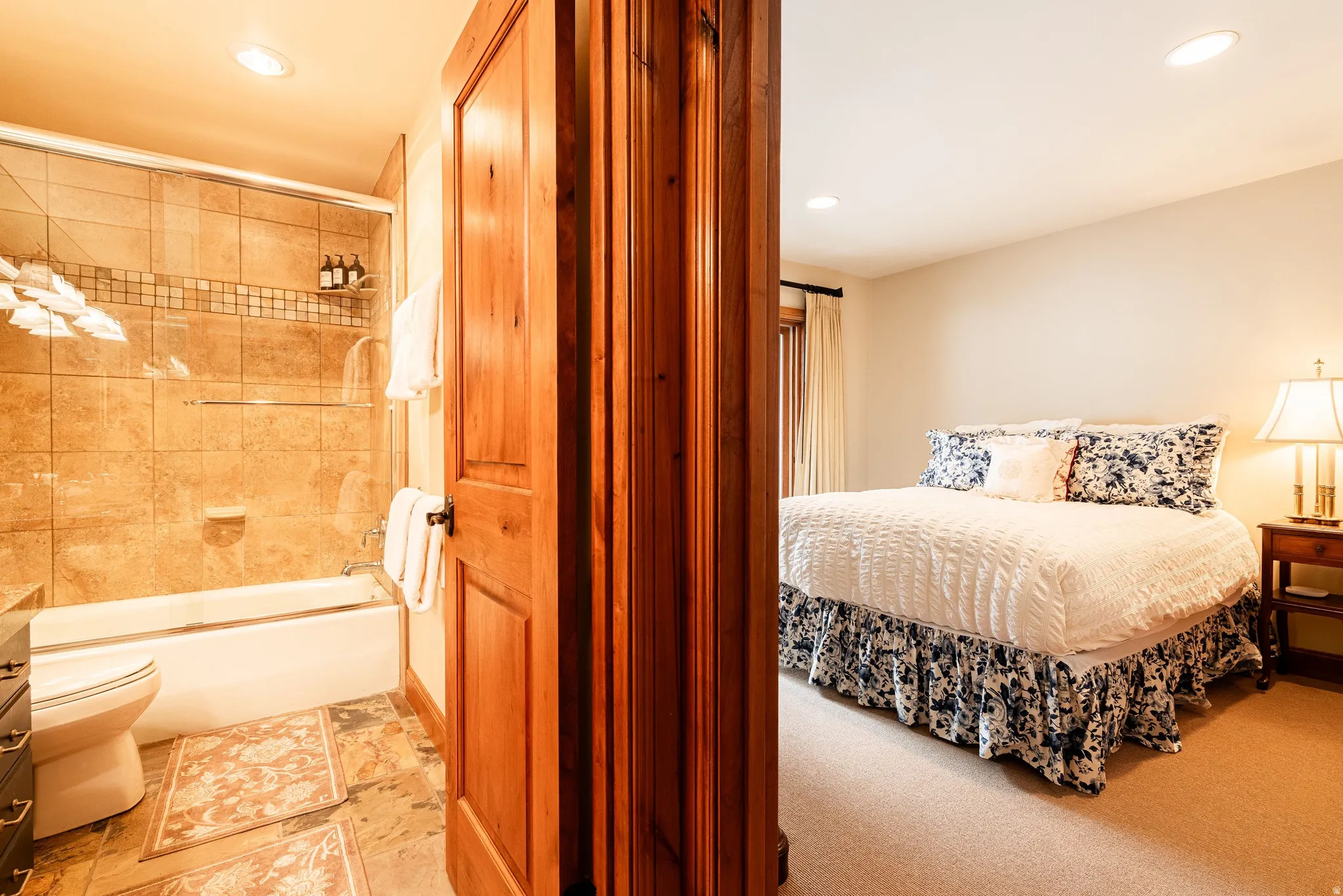 Bathroom featuring a tiled shower/tub combination with glass enclosure, natural wood door, and recessed lighting