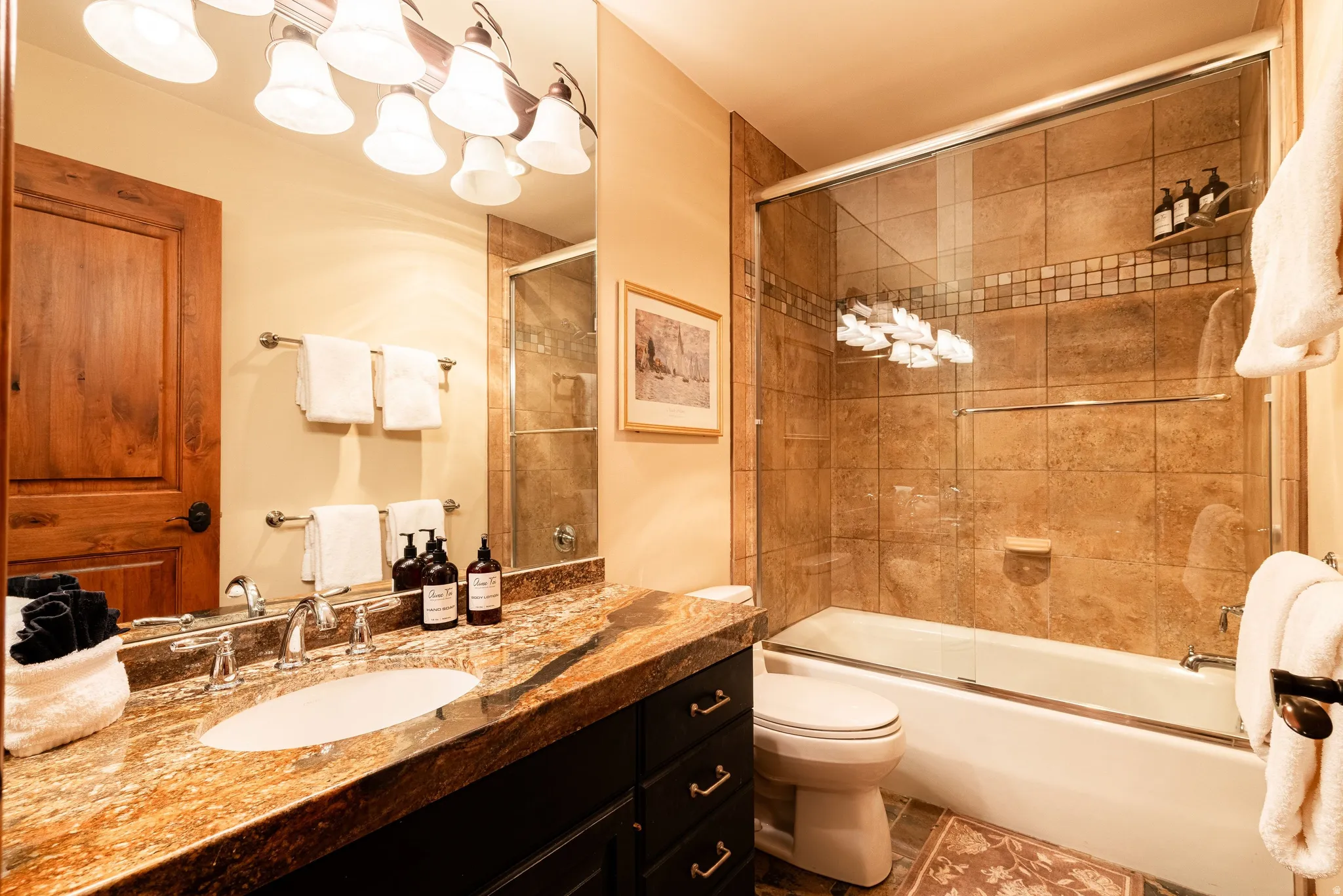 Bathroom featuring a bathtub with a glass shower enclosure, stone tile surround, and decorative tile accent band