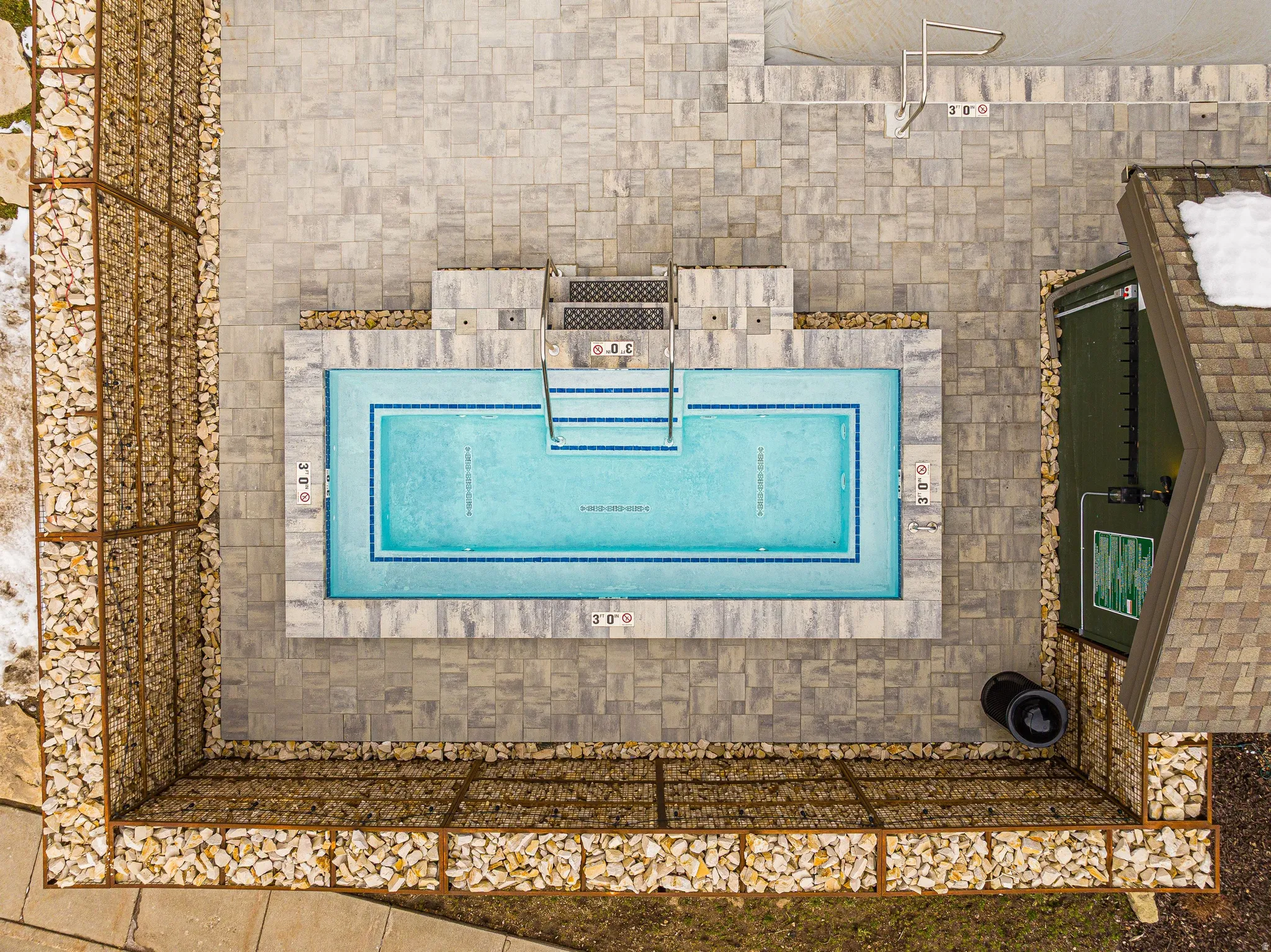 Rectangular swimming pool with blue tile accents, surrounded by an expansive paver patio
