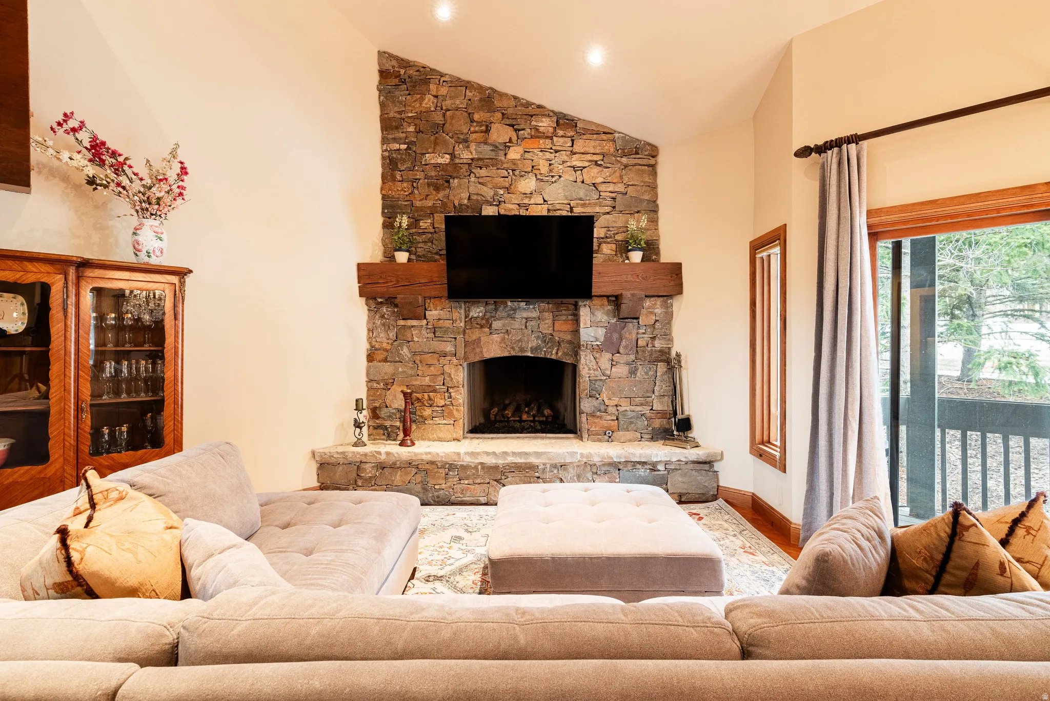 Stone fireplace with a substantial timber mantel and hearth, recessed lighting, wood-trim doorway, and outdoor balcony access