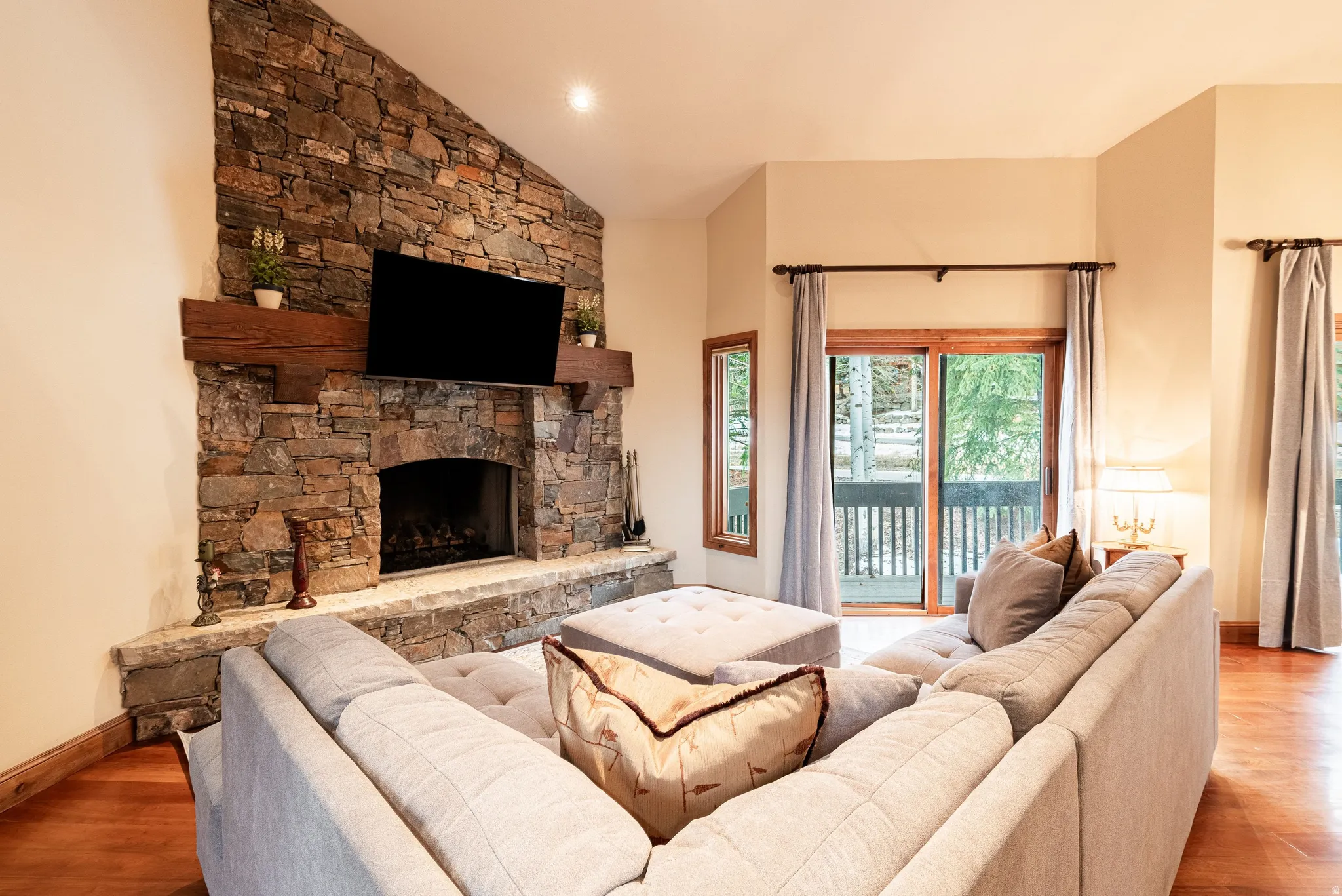 Vaulted living area featuring a stone fireplace with a wood mantle, hardwood flooring, and a sliding glass door opening to an exterior deck
