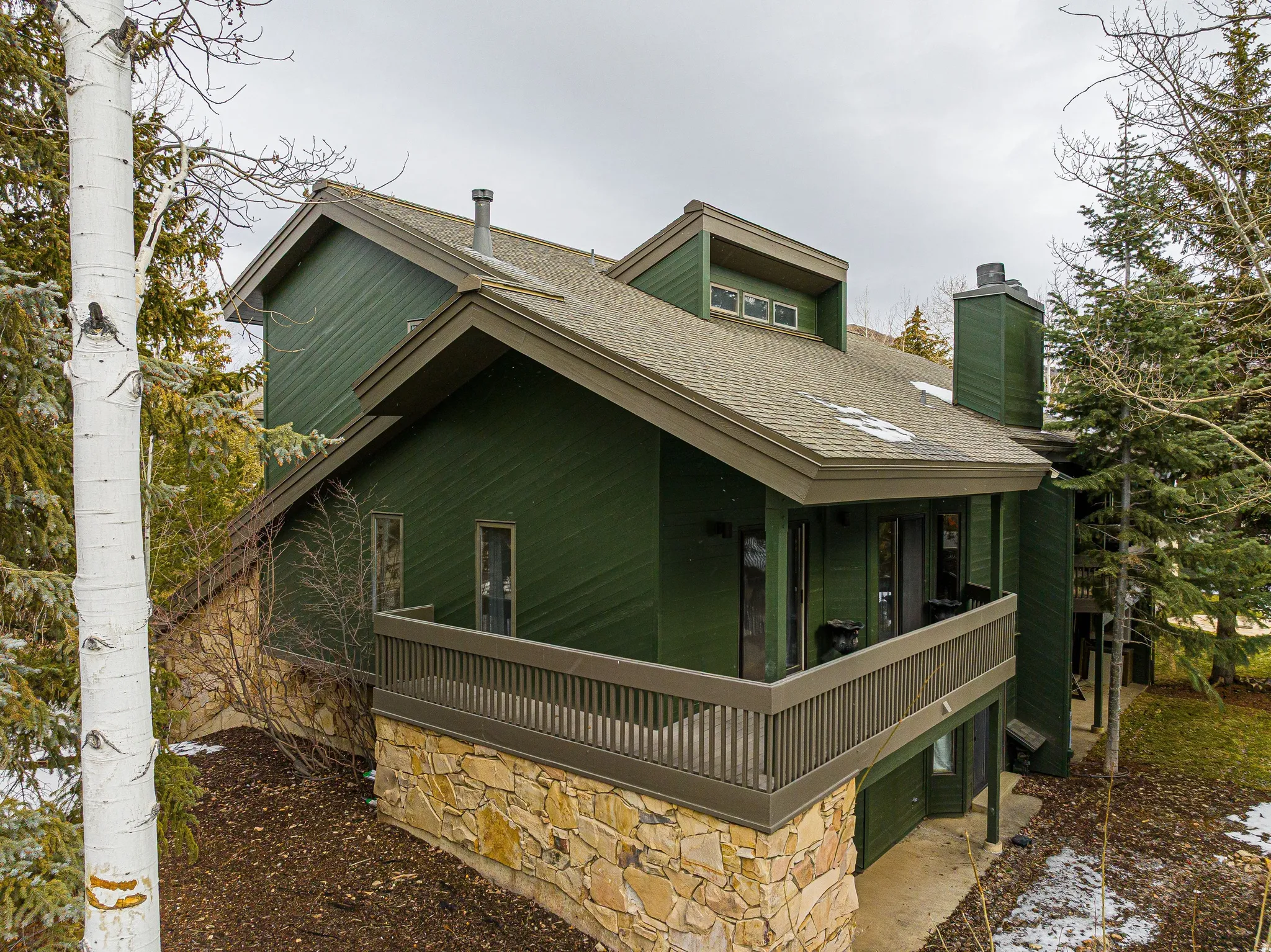 Multi-level exterior featuring a stone foundation, wood siding, and a prominent balcony with a wooden railing