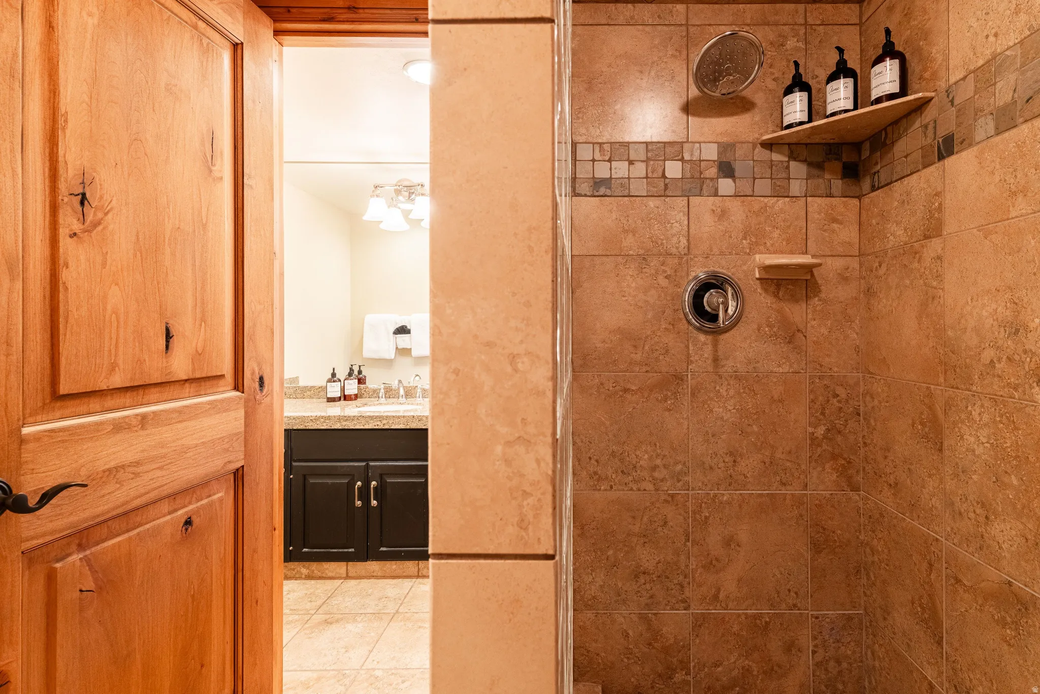 Tiled shower enclosure featuring a mosaic accent band, integrated corner shelf, and a rain showerhead