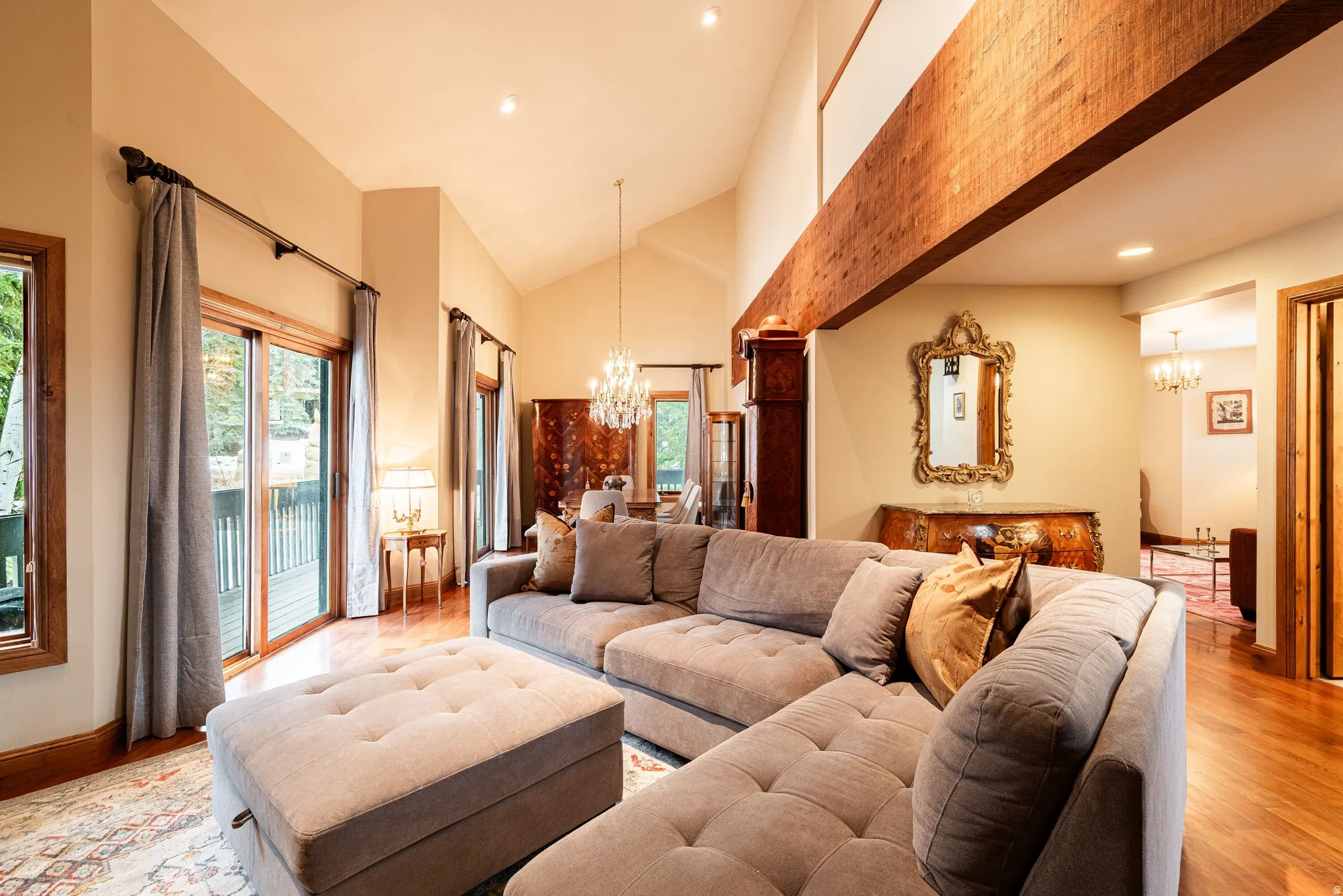 Spacious living area featuring high vaulted ceilings, warm wood-finish flooring, and expansive glass sliding doors opening to an exterior deck