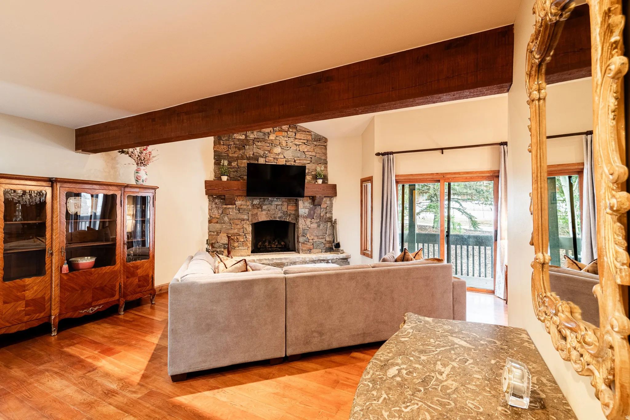 Vaulted ceiling with exposed wood beam and a stone-clad fireplace featuring a wood mantle