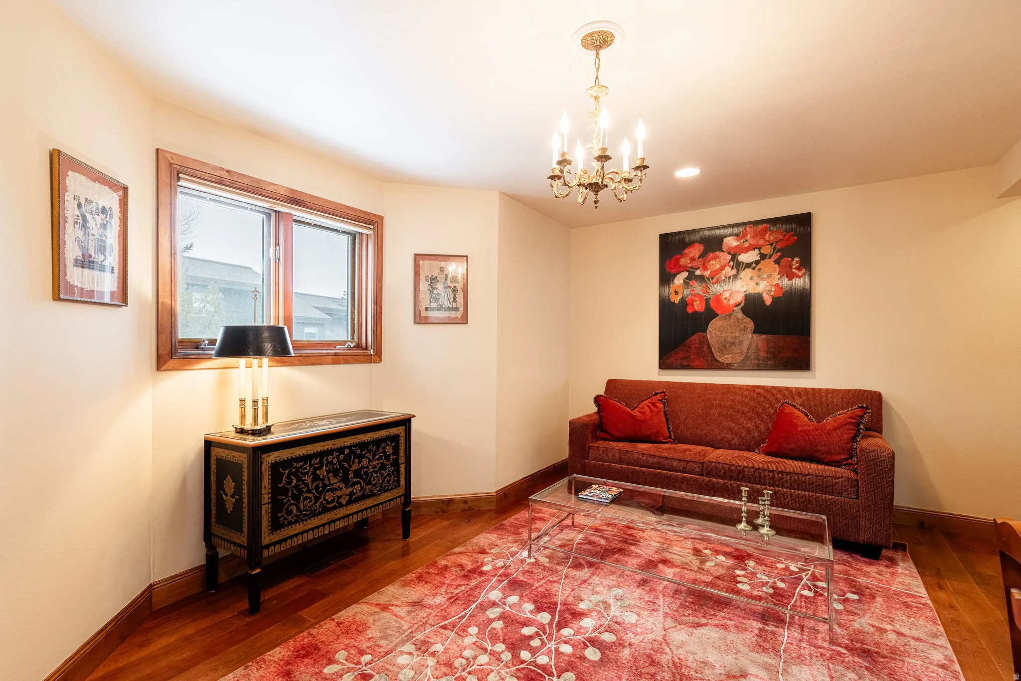 Room featuring wood-finish flooring, a window with wood trim, and a brass chandelier