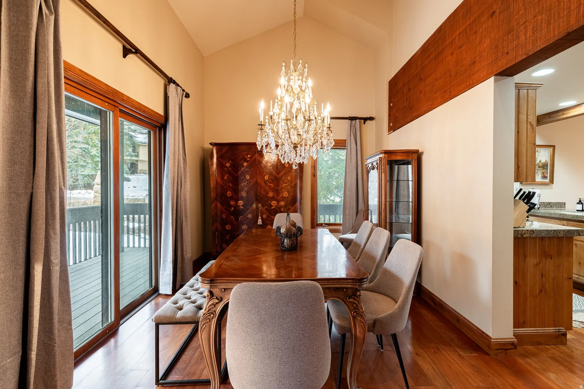 Dining area featuring a vaulted ceiling with a crystal chandelier, wood-finish flooring, and sliding glass doors opening to an exterior deck