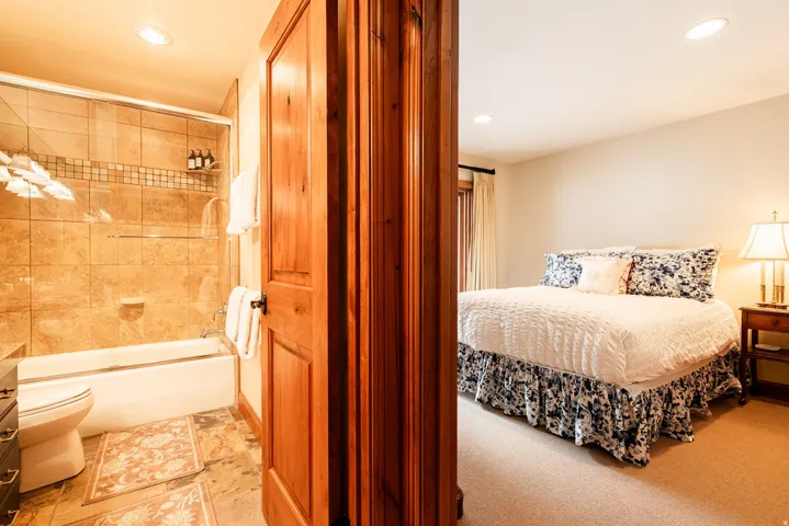Bathroom featuring a tiled shower/tub combination with glass enclosure, natural wood door, and recessed lighting