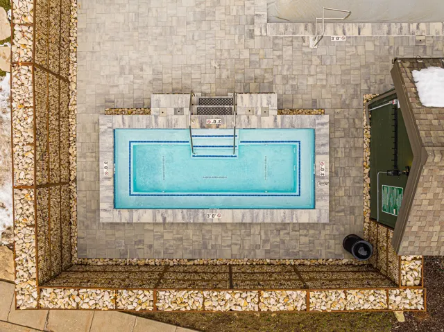 Rectangular swimming pool with blue tile accents, surrounded by an expansive paver patio