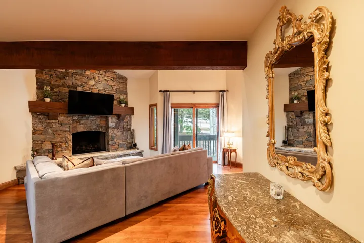 Living space featuring a stone-clad corner fireplace with a wood mantle, exposed wood ceiling beam, and wood-finish flooring