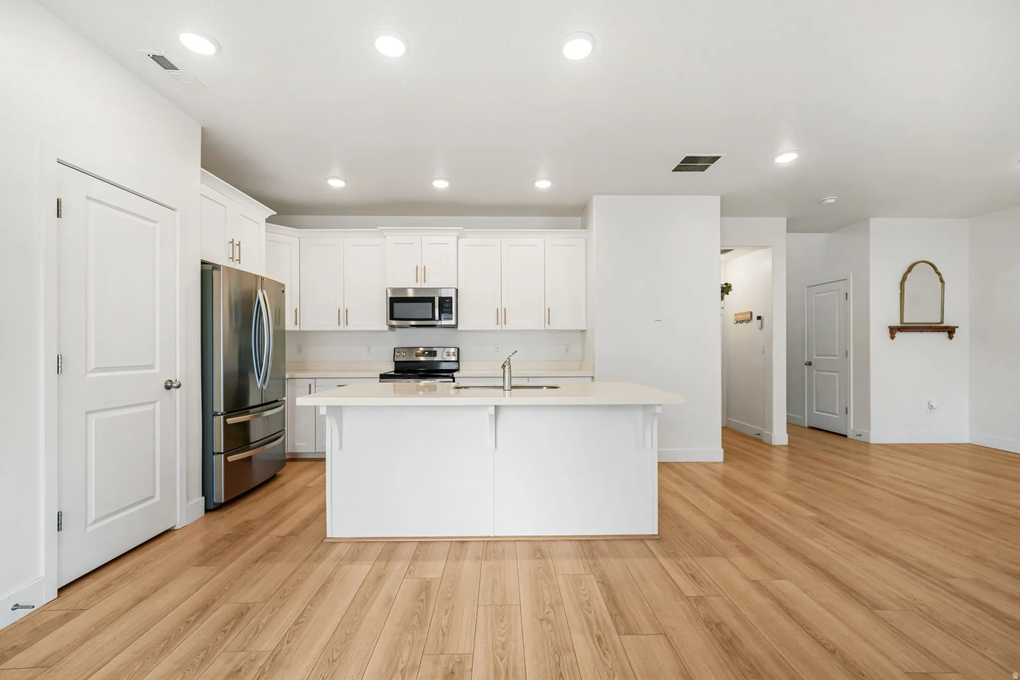 Modern kitchen featuring white cabinetry, stainless steel appliances, and a central island with a sink