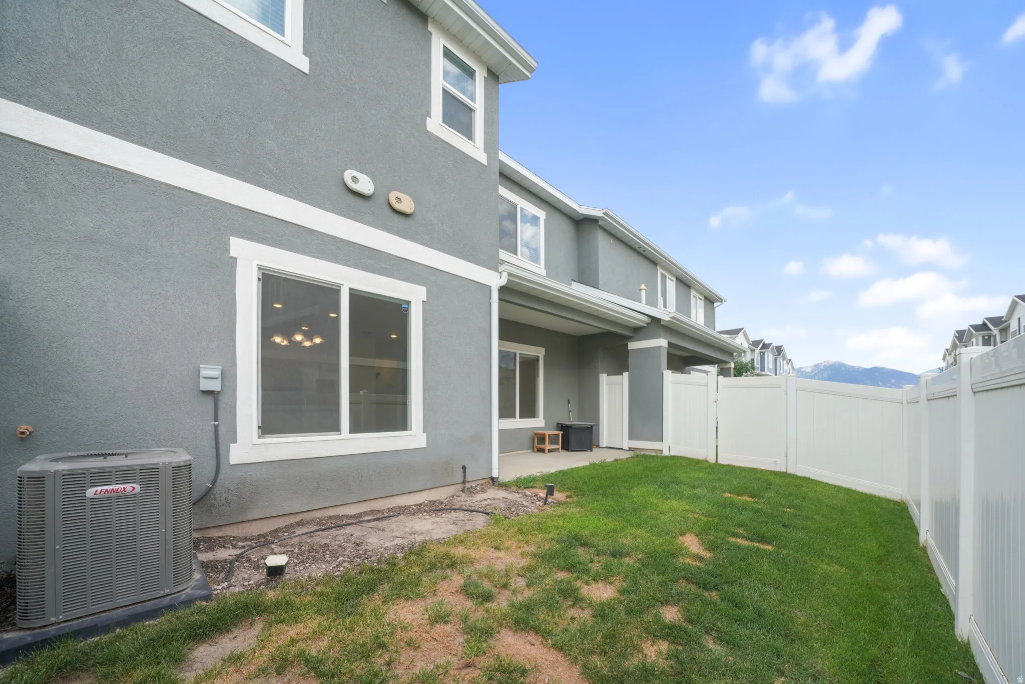 Expansive green lawn area featuring a white privacy fence, a concrete patio, and mountain scenery in the distance