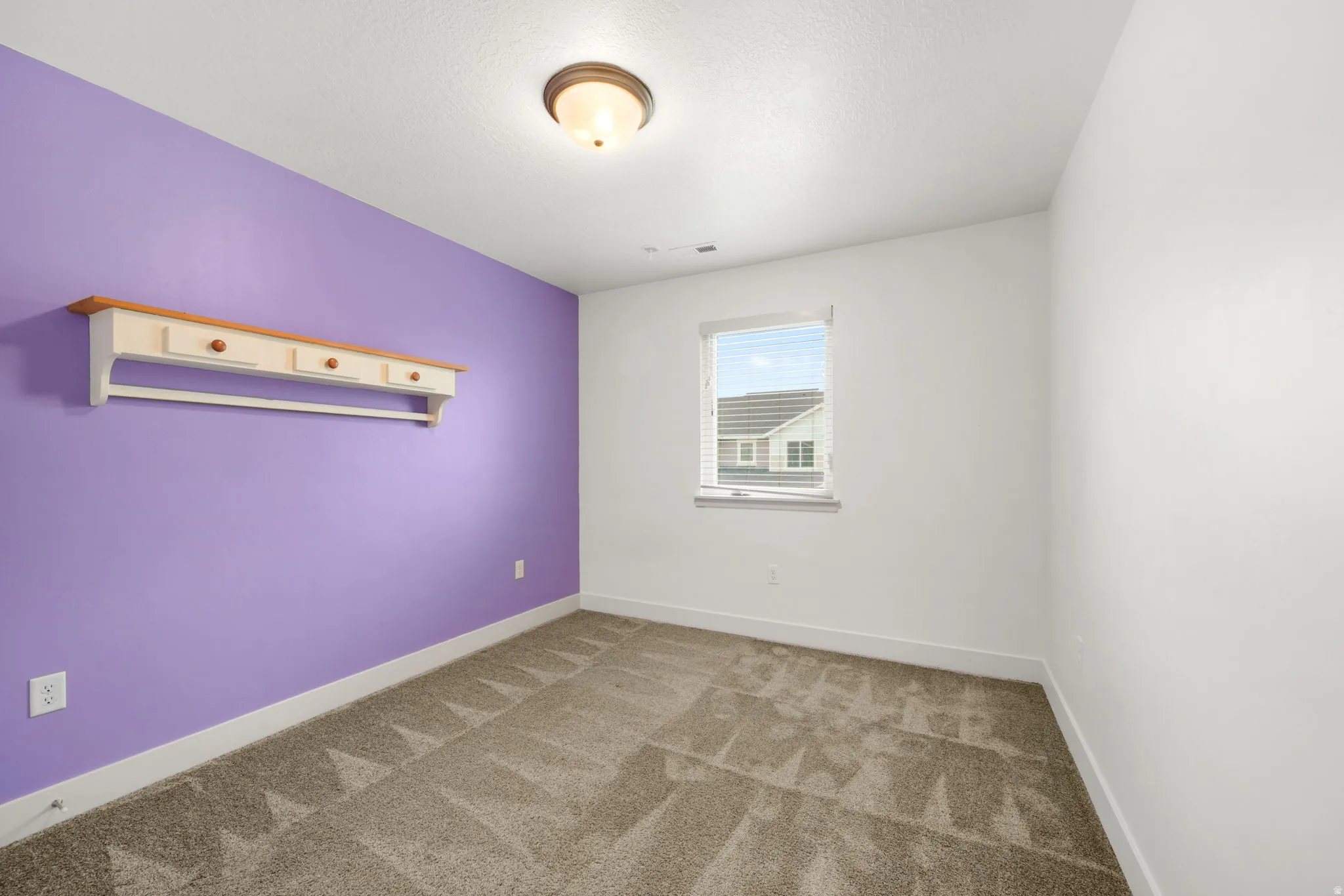 Room featuring a single window with blinds, a ceiling-mounted light fixture, and textured carpet flooring