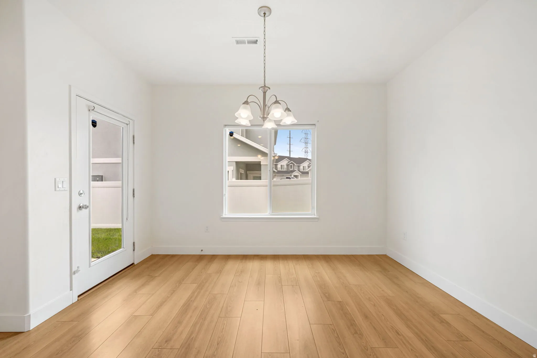 Open-concept room featuring wood-finish flooring, a contemporary chandelier, a single window, and a glass-paneled door providing outdoor access