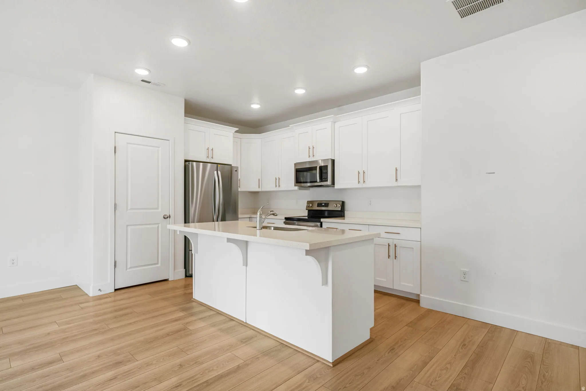Modern kitchen featuring a central island, white cabinetry, stainless steel appliances, and wood-finish flooring