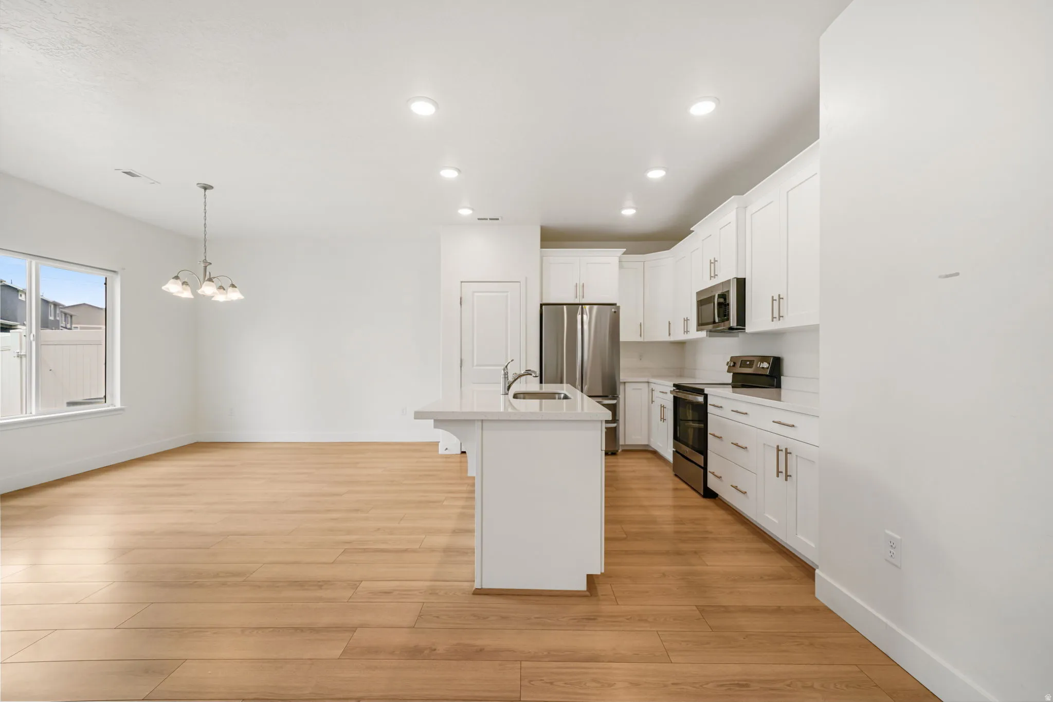 Open concept living area featuring light wood-finish flooring, recessed lighting, and a kitchen with white cabinetry