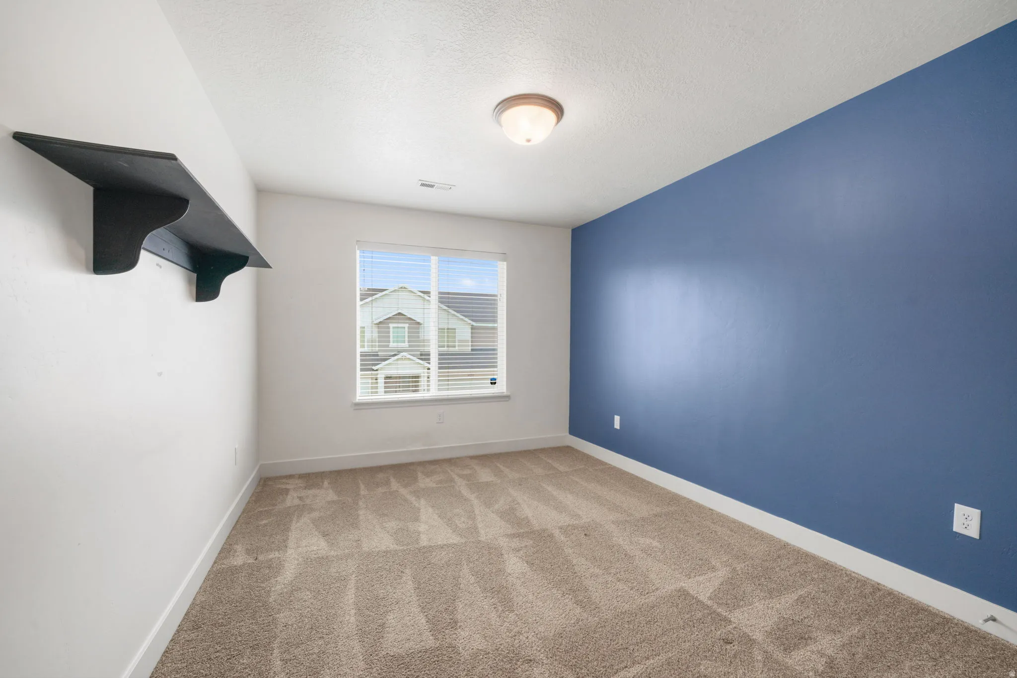 Bright room featuring a single window with blinds, a built-in wall shelf, a flush mount ceiling light, and neutral carpet flooring