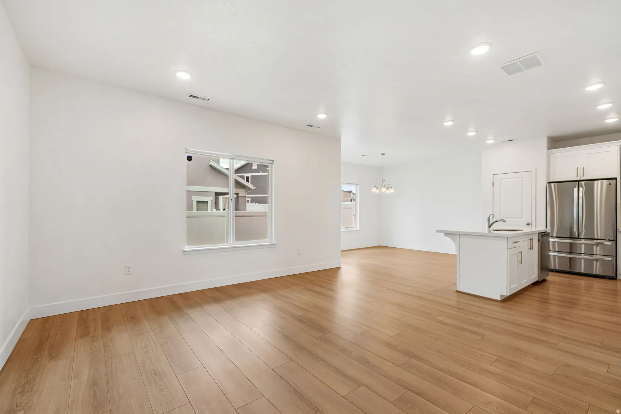 Open-concept living area featuring light wood-finish flooring, recessed lighting, and a kitchen island with sink