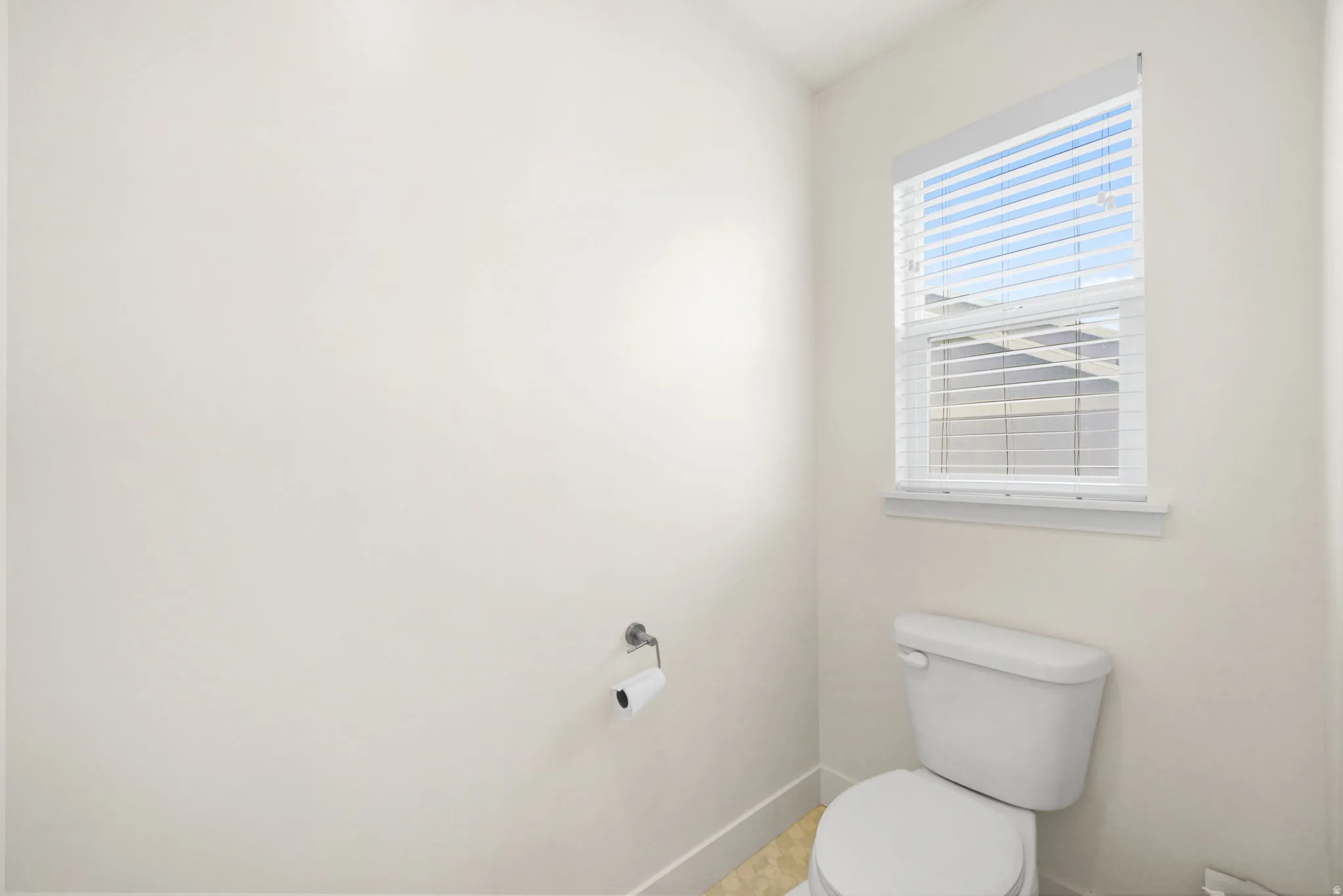 Compact bathroom featuring a white toilet, neutral wall paint, a window with blinds, and tile flooring