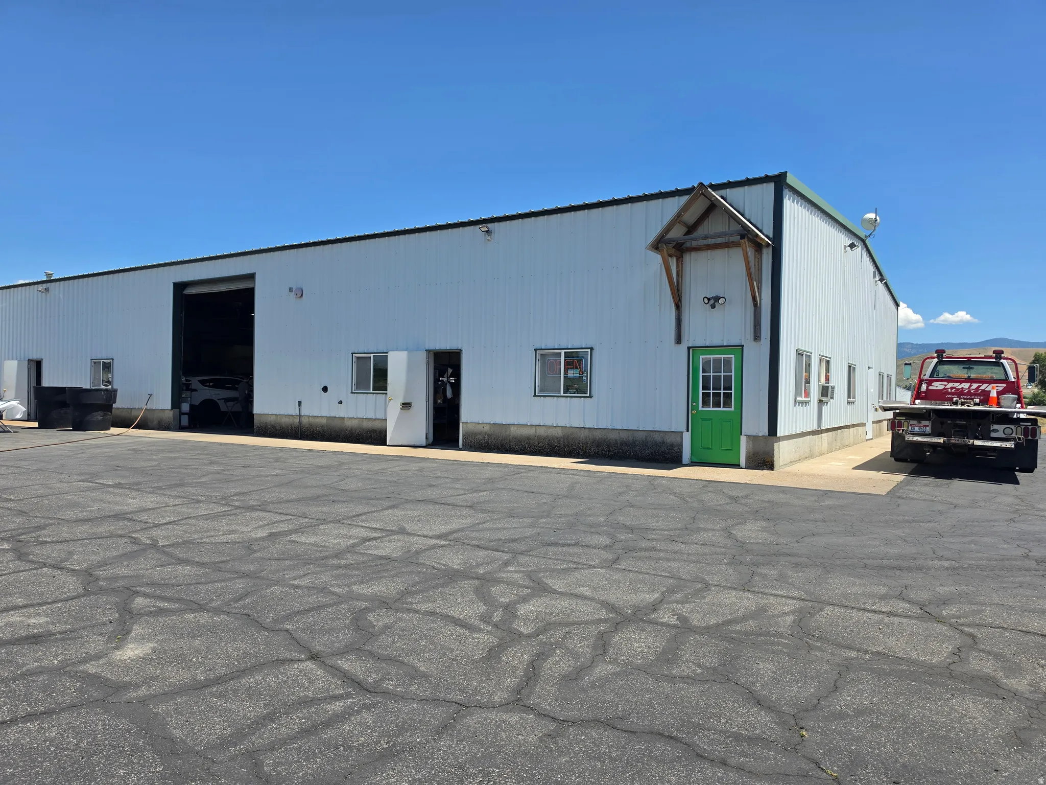 Metal-sided commercial building featuring a large overhead door, multiple pedestrian entrances, and a paved lot