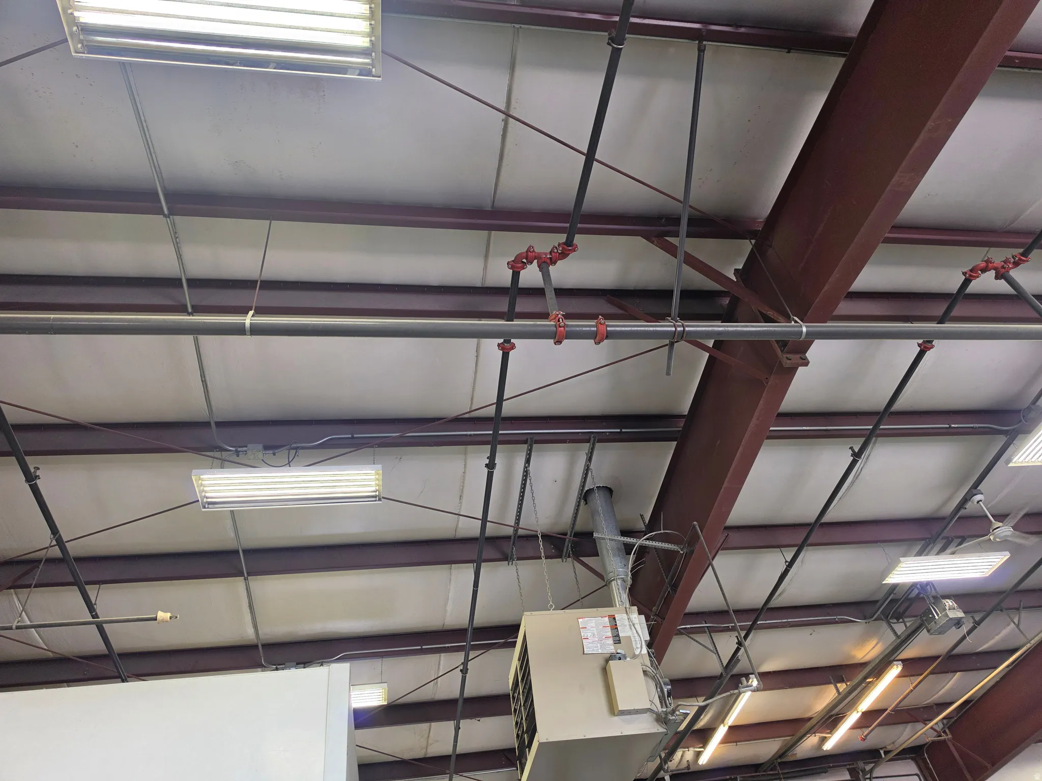 Exposed ceiling structure featuring steel I-beams, extensive conduit, and multiple fluorescent light fixtures With full fire suppression.