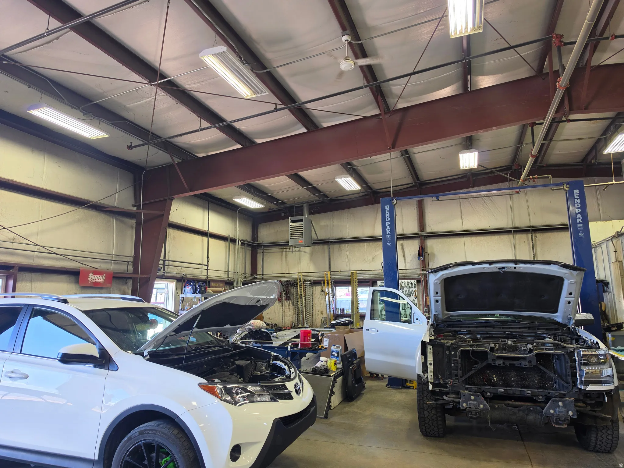 Spacious commercial interior featuring exposed steel I-beams, multiple fluorescent light fixtures, two vehicle lifts, and a concrete floor