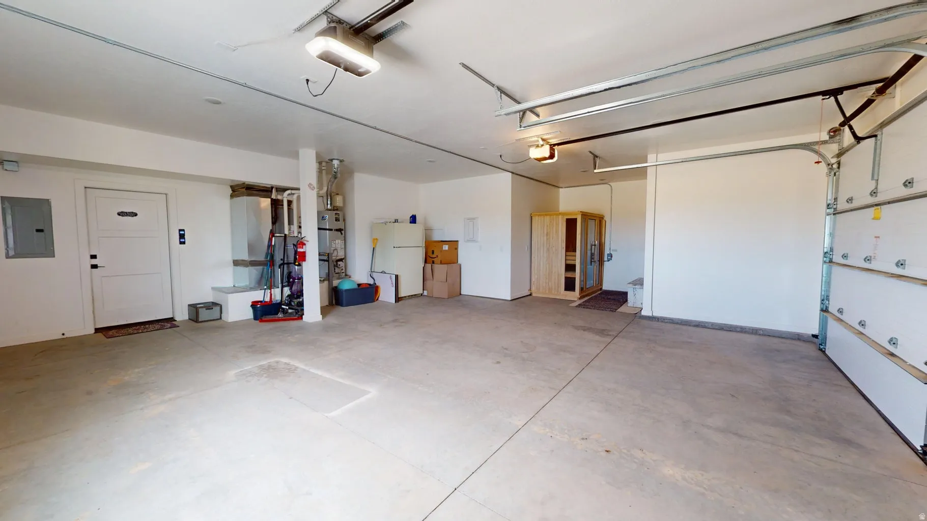 Spacious garage featuring a concrete floor, overhead lighting, and an integrated sauna unit