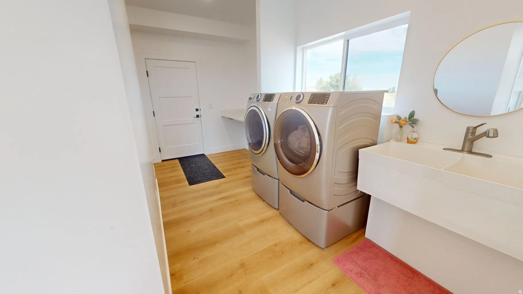 Spacious laundry area featuring wood-finish flooring, a large window, a three-panel door, and a built-in utility sink with a single-handle faucet