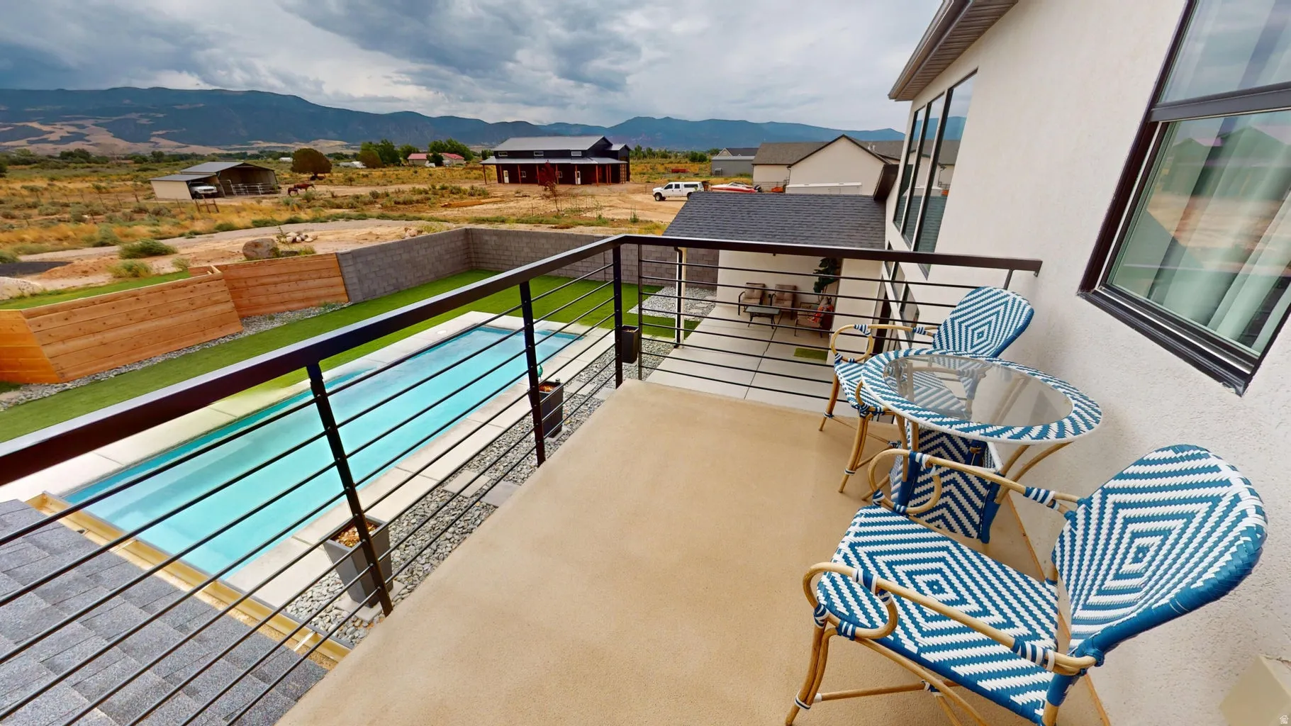 Balcony with cable railing overlooking a rectangular pool, synthetic turf, and a stone wall