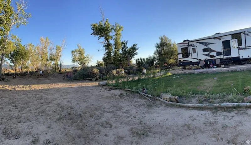Expansive outdoor space featuring a large unpaved area, mature trees, and a grassy section
