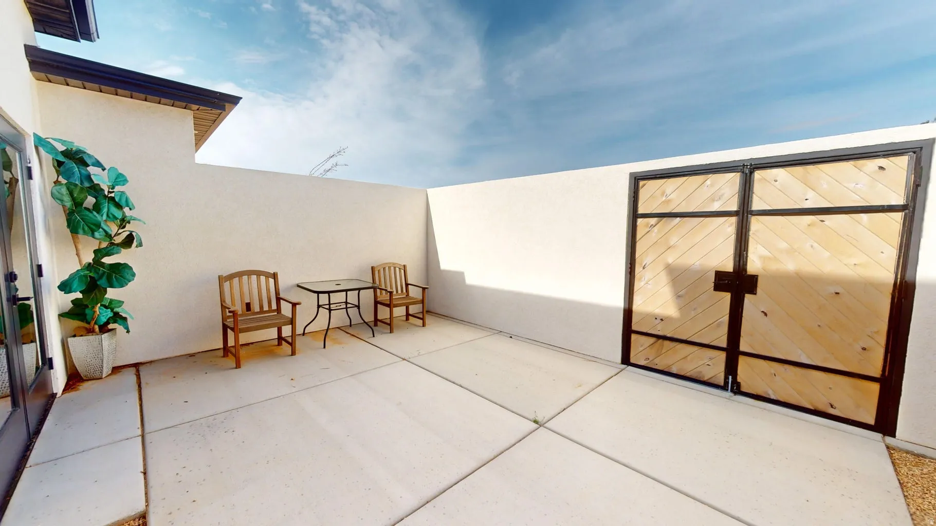 Private courtyard featuring a wood-panel gate with metal framing, concrete patio, stucco walls, and French patio doors