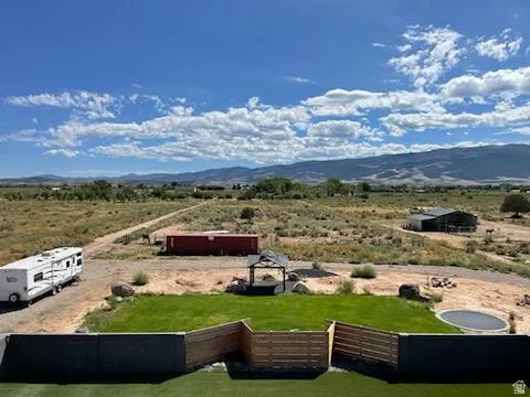 Expansive outdoor space featuring a manicured lawn, a circular in-ground trampoline, a pergola, and a dark-colored storage building in the distance