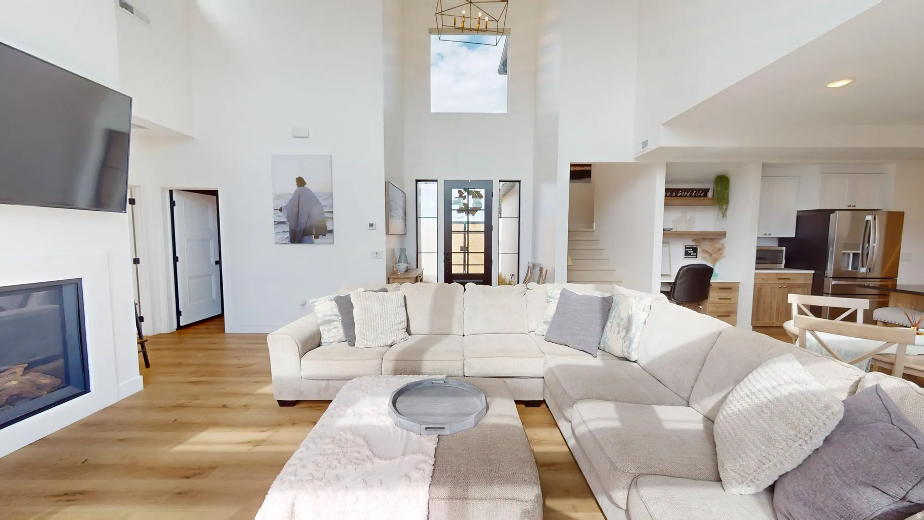 Spacious living area featuring high ceilings, wood-finish flooring, a built-in fireplace with a white mantel, and a prominent front entry with dark-framed glass doors