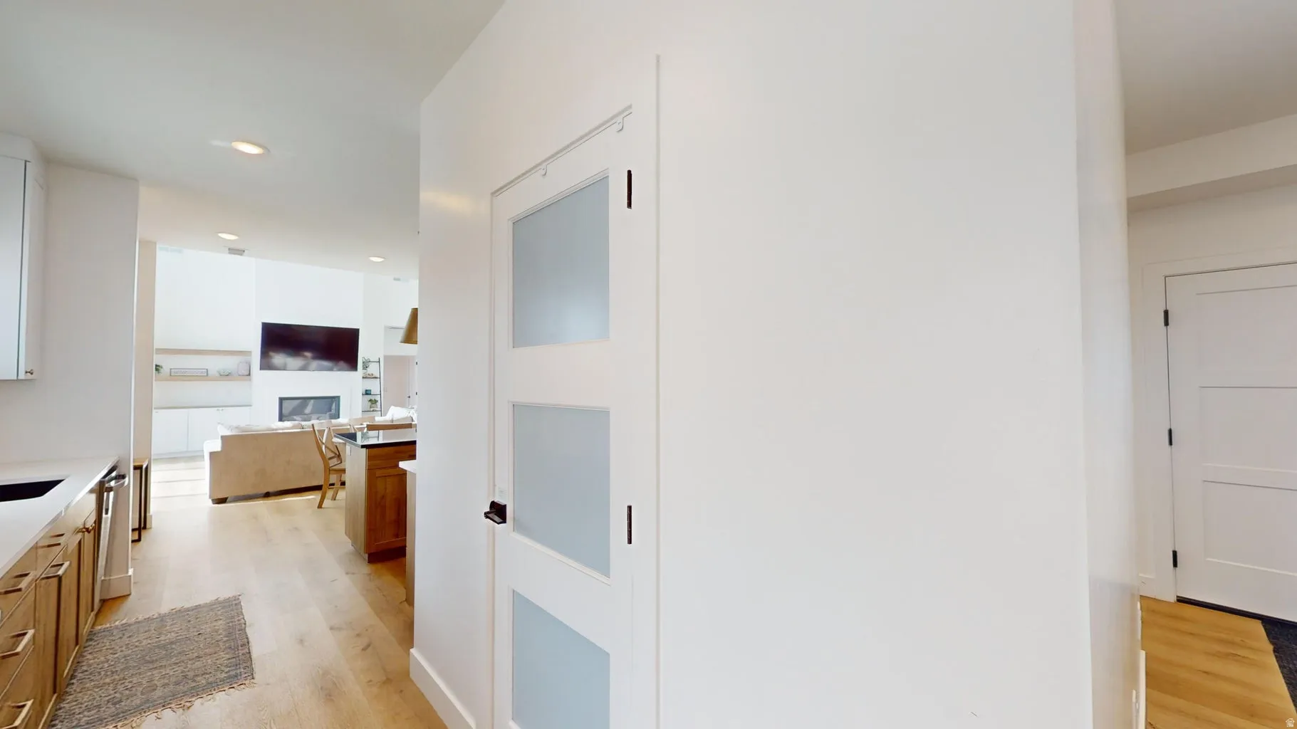 Three-panel frosted glass interior door with dark hardware, recessed ceiling lighting, light wood-finish flooring, and white baseboards