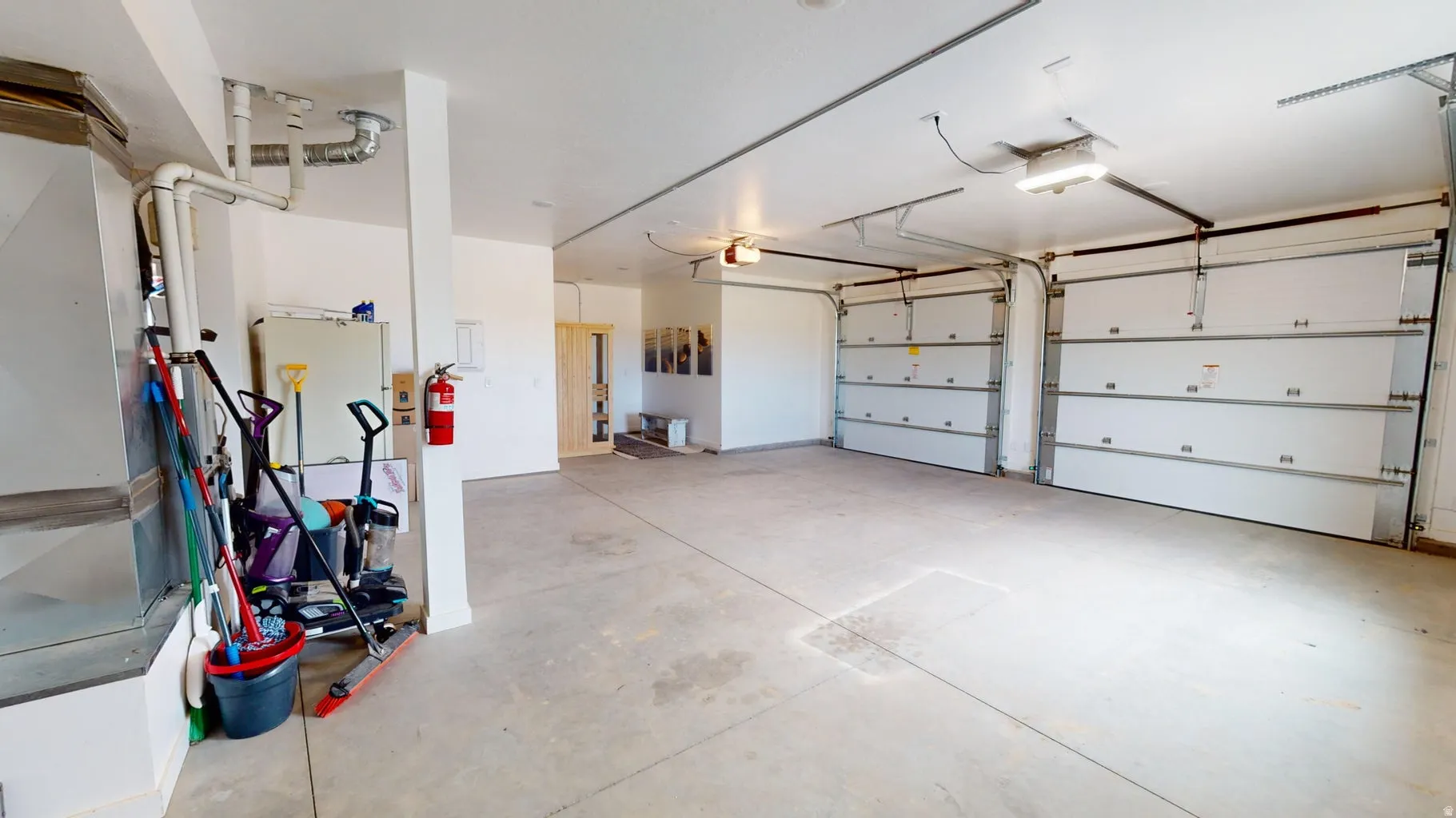 Spacious garage featuring a concrete floor, two white overhead garage doors, exposed ductwork, and fluorescent lighting fixtures