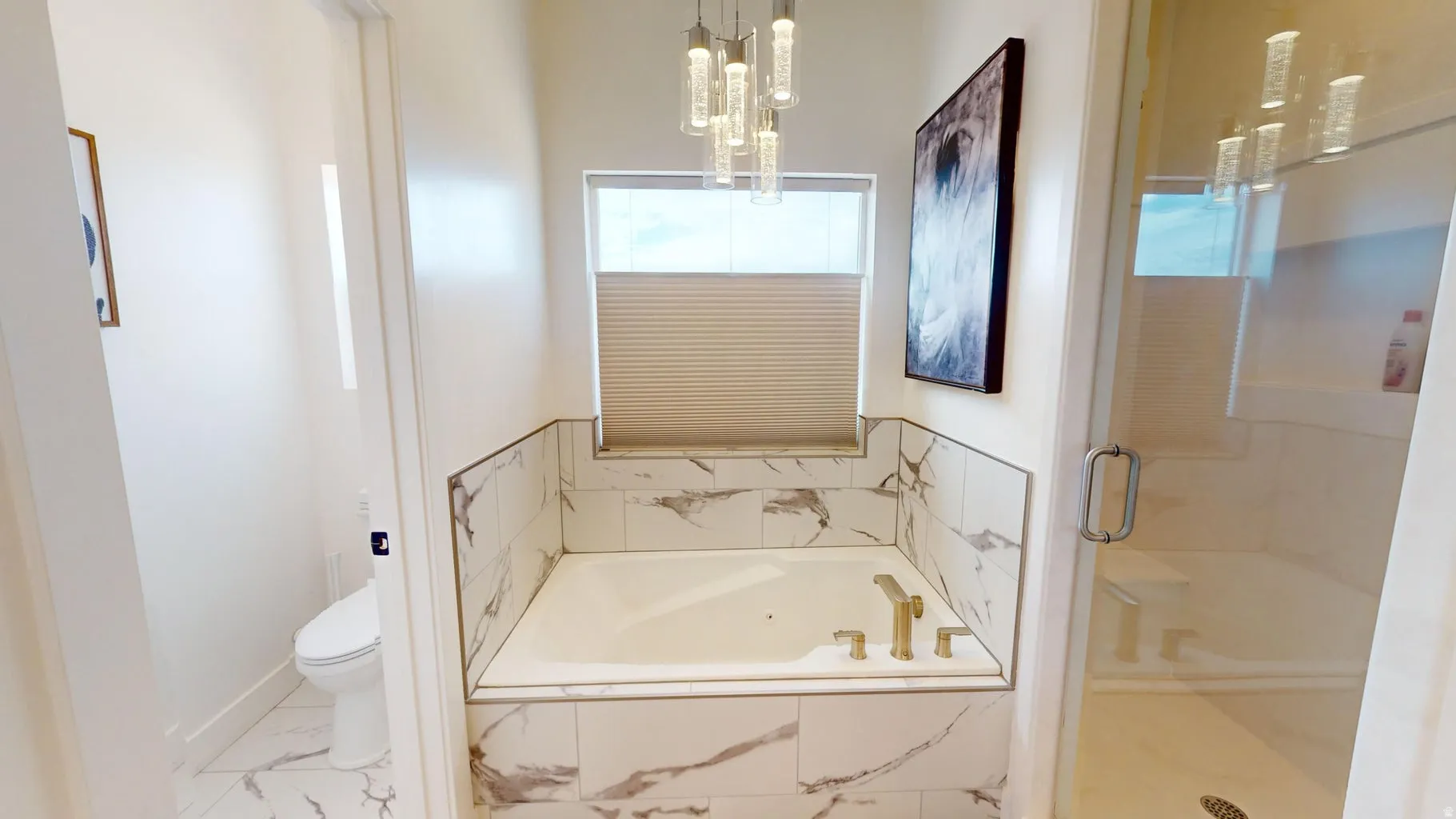 Soaking tub with gold-tone fixtures and surrounding marble-look tile