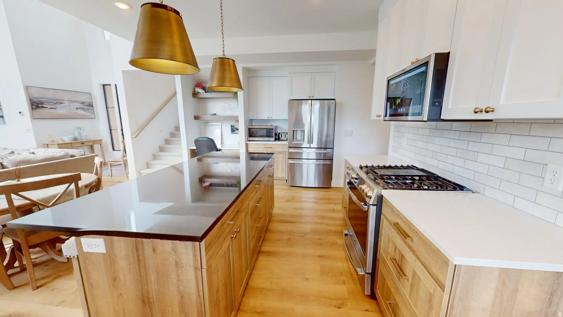 Modern kitchen featuring a large island with a dark countertop, white shaker cabinetry, stainless steel appliances, and wood-finish flooring