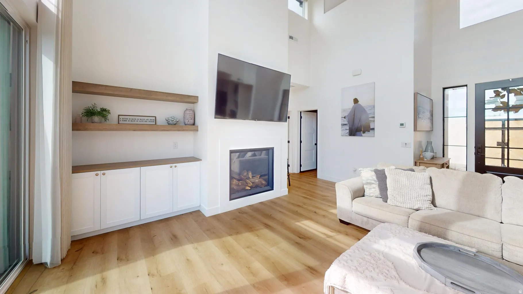 Great room featuring high ceilings, a built-in fireplace, wood-finish flooring, and integrated white cabinetry with wood-finish shelving