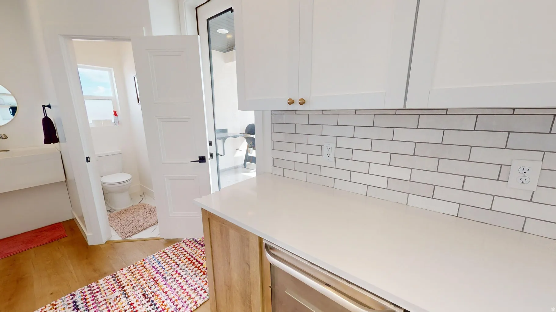 Modern kitchen counter featuring white upper cabinetry with gold-tone hardware, a light-toned countertop, and a subway tile backsplash