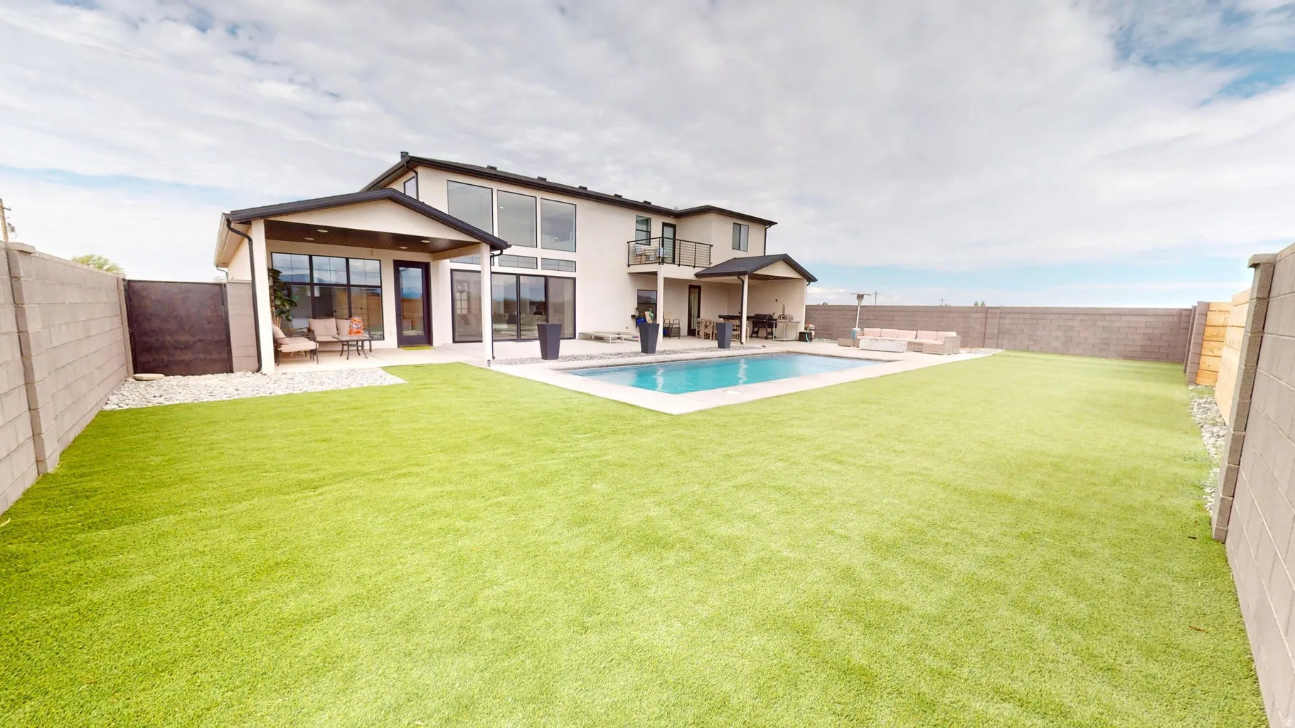 Expansive backyard featuring a large swimming pool, an artificial turf lawn, and a covered patio