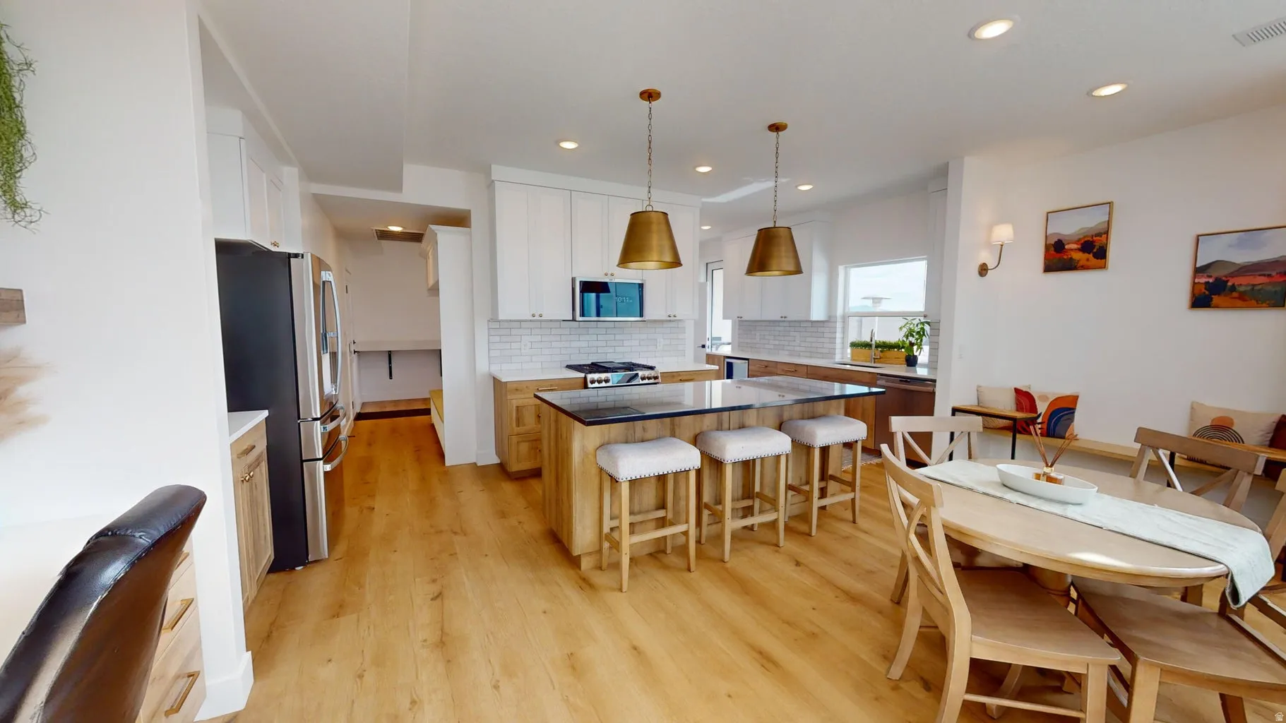 Open-concept kitchen and dining area featuring light wood-finish flooring, a kitchen island with dark countertops, white shaker-style cabinetry, and stainless steel appliances