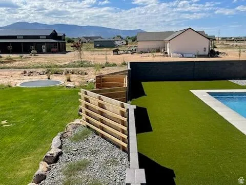Backyard featuring a rectangular swimming pool with light-colored coping, artificial turf, and a dark privacy fence