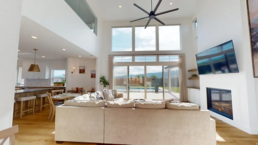 Two-story living area with high ceilings, wood-finish flooring, and a contemporary ceiling fan