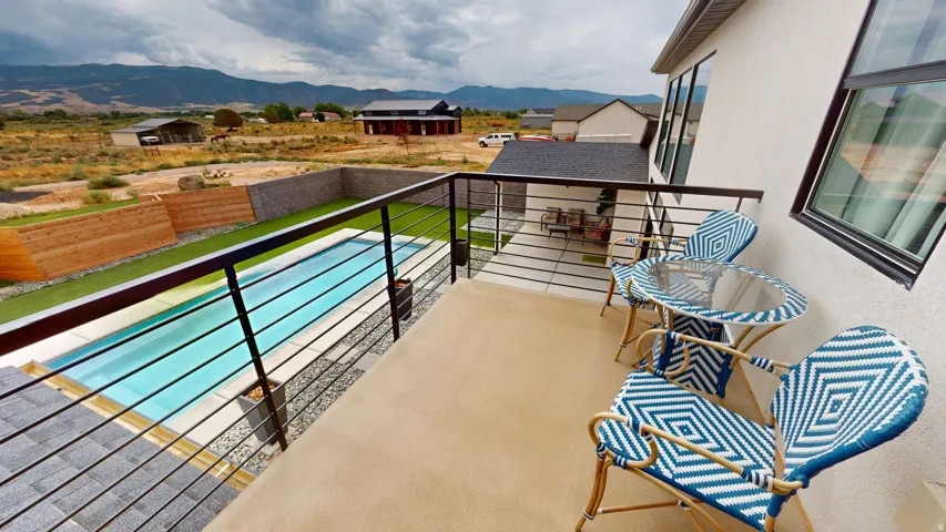 Balcony with cable railing overlooking a rectangular pool, synthetic turf, and a stone wall