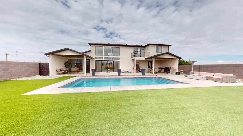 Spacious backyard featuring a rectangular swimming pool with integrated steps, expansive artificial turf lawn, and a large concrete patio